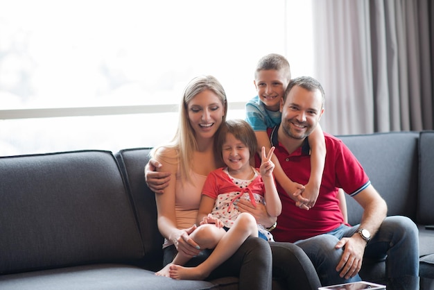 Família jovem feliz jogando junto com o tablet em casa sentado no sofá