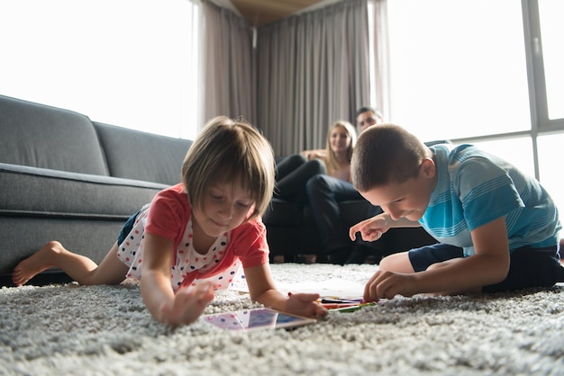 Família jovem feliz jogando juntos em casa no chão usando um tablet e um conjunto de desenho infantil