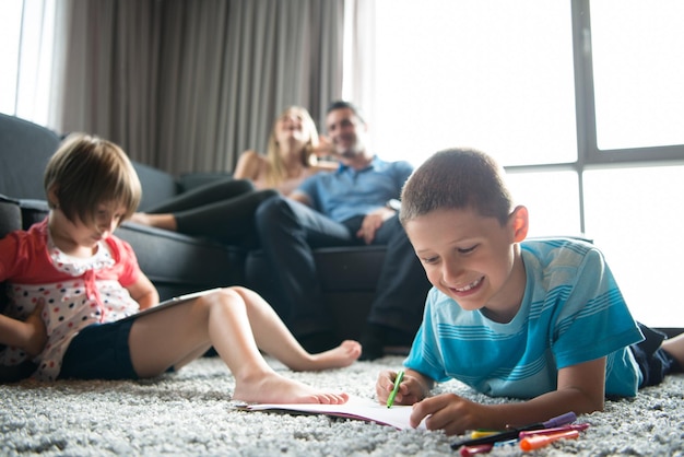 Família jovem feliz jogando juntos em casa no chão usando um tablet e um conjunto de desenho infantil