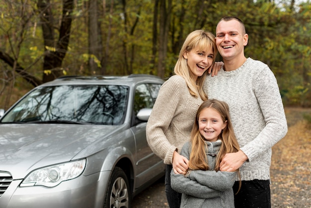 Foto família jovem feliz, posando ao lado de um carro