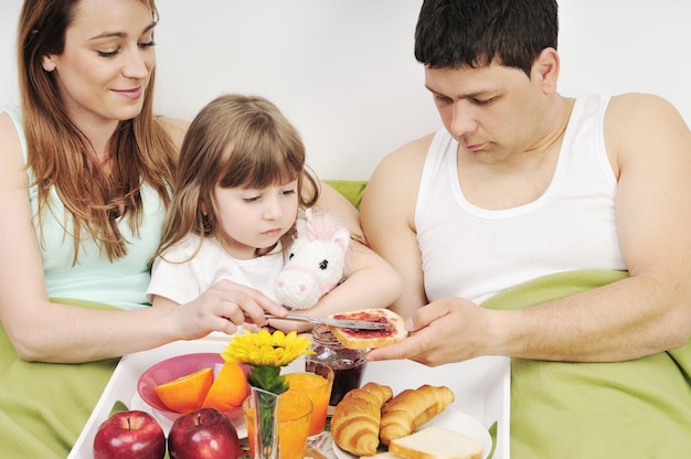 família jovem feliz toma café da manhã na cama de manhã