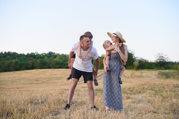 Foto família jovem feliz. um pai, uma mãe grávida e dois filhos pequenos nas costas. campo de trigo chanfrado