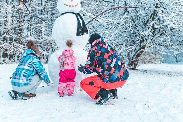 Família jovem jogando no parque da cidade de inverno. fazendo boneco de neve. o Natal está chegando