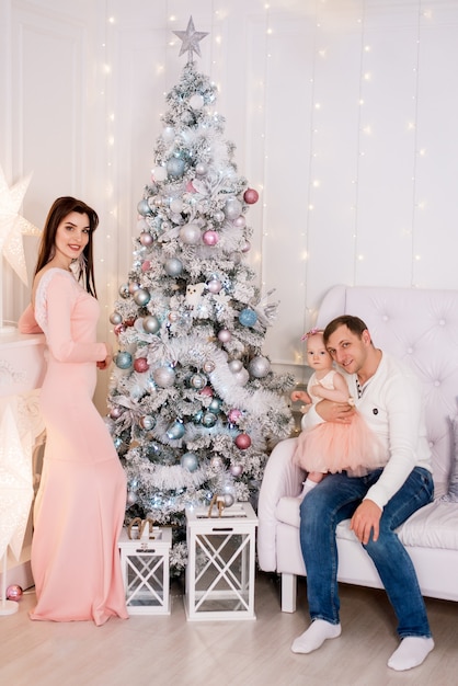 Família jovem. Mãe, pai e filha decoram a árvore de Natal.