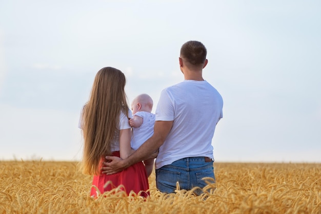 Família jovem no campo de trigo com criança pequena, mãe, pai e bebê, vista traseira