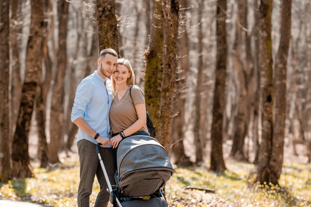 Família jovem passeio no parque na primavera com uma criança em um carrinho. Pais felizes