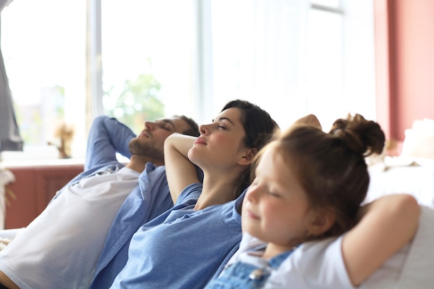 Família jovem relaxada, descansando e sonhando com a nova casa no sofá confortável juntos em casa, pais jovens felizes com a filha pequena relaxam desfrutando de um cochilo, relaxando ou meditando.