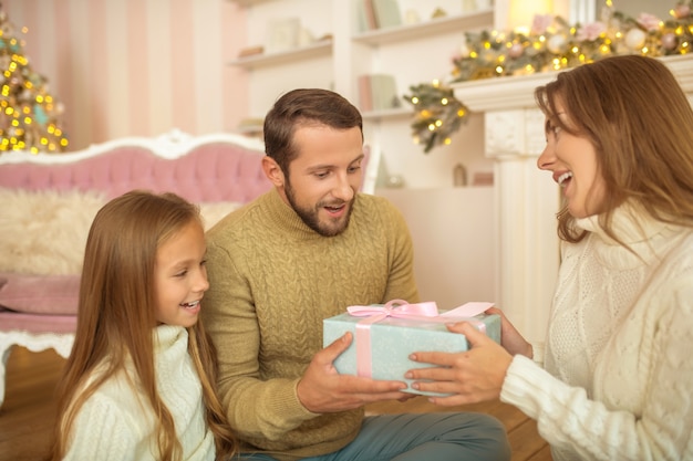 Família jovem sentada no chão trocando presentes de Natal