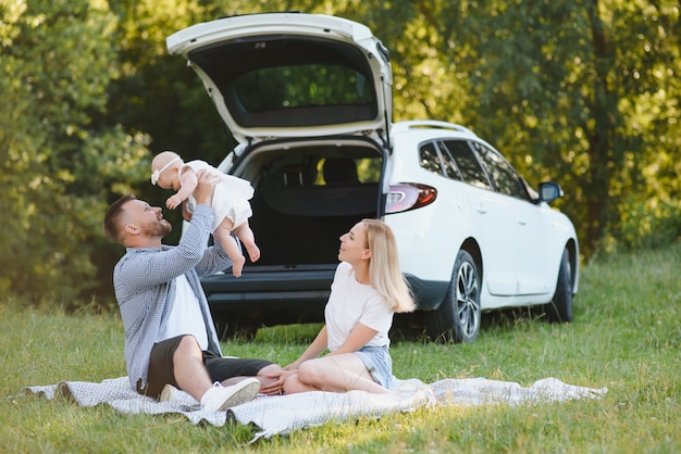 Família jovem três pessoas em roupas brancas fazem piquenique. filha e pais lindos viajam de carro durante as férias de verão.