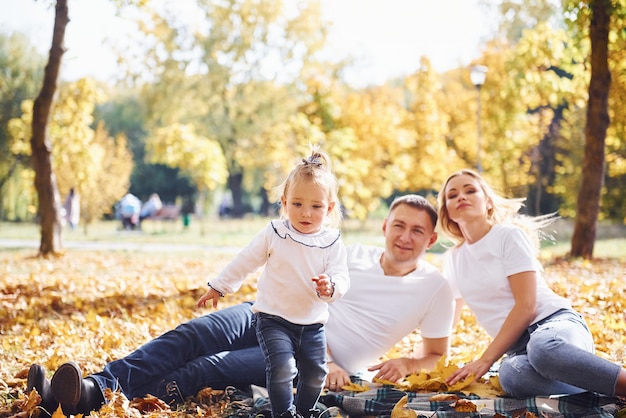 Familia joven alegre acostado en el suelo y descansar juntos en un parque de otoño.