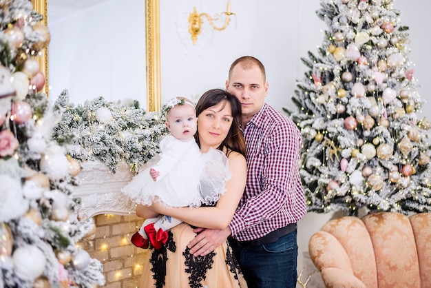 Una familia joven con un bebé en brazos contra los árboles de Navidad cubiertos de nieve.