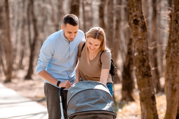 Familia joven caminar en el parque en la primavera con un niño en un cochecito. Padres felices