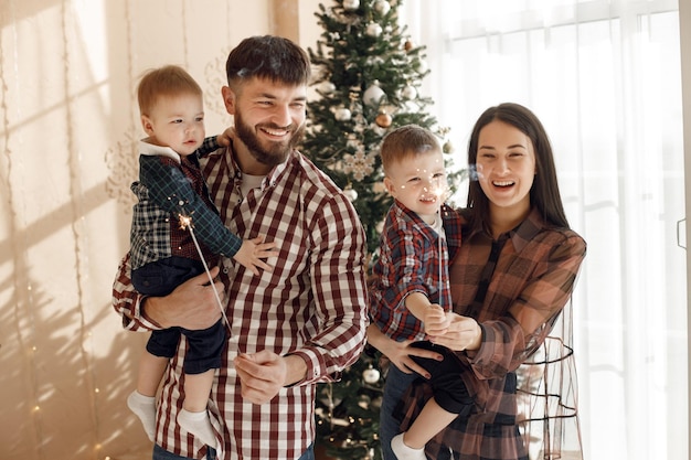 Familia joven en camisas a cuadros de pie cerca del árbol de Navidad con bengalas