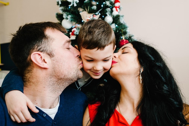 Familia joven celebrando la Navidad en casa cerca del árbol de Navidad Feliz mamá papá e hijo disfrutando juntos de sus vacaciones