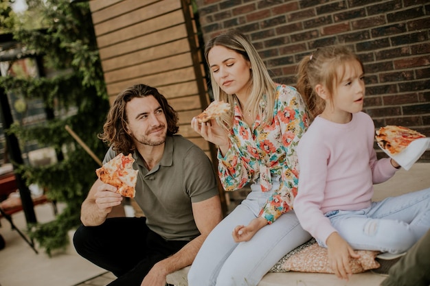 Familia joven comiendo pizza en el patio trasero de la casa