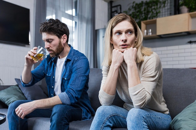 Una familia joven se desmorona a una mujer deprimida debido a una pareja de esposos alcohólicos sentados en un sofá en la sala de estar