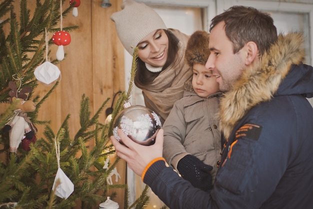 Familia joven disfrutando de sus vacaciones juntos, decorando el árbol de Navidad en la guerra