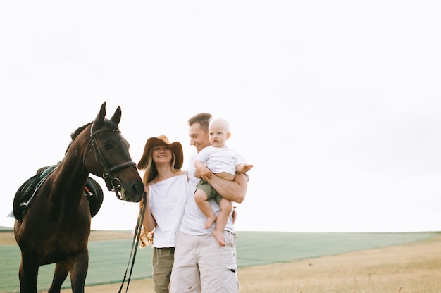 Una familia joven se divierte en el campo. Padres e hijo con un caballo