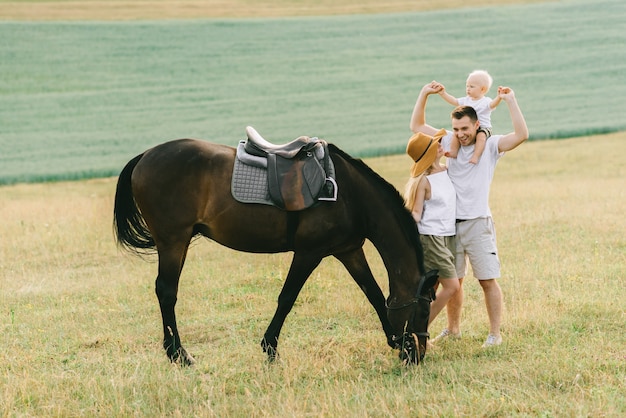 Una familia joven se divierte en el campo. Padres e hijos con un caballo
