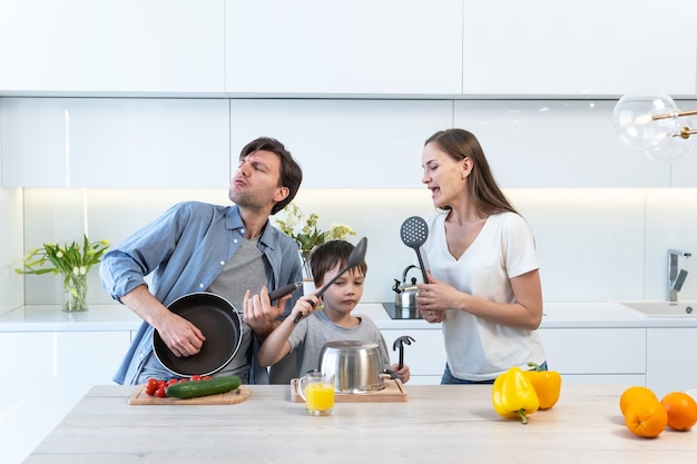 Familia joven divirtiéndose, bailando y cantando en la cocina