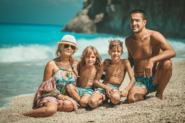 Una familia joven con dos hijos está posando en la playa del mar en el día de verano y mirando la cámara.