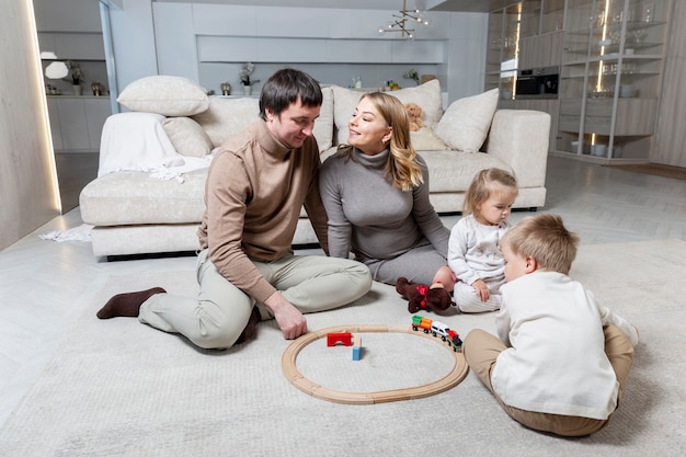 Una familia joven con dos niños pequeños está sentada en el suelo de la sala de estar. Tiempo feliz juntos. Amor y ternura.
