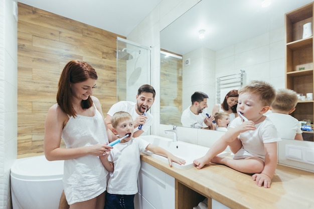 Familia joven con dos niños pequeños que se divierten cepillándose los dientes juntos en el baño