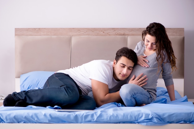 Familia joven con esposa embarazada esperando bebé en la cama