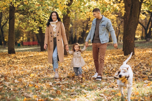 Familia joven feliz camina y juega con un perro en el parque de otoño