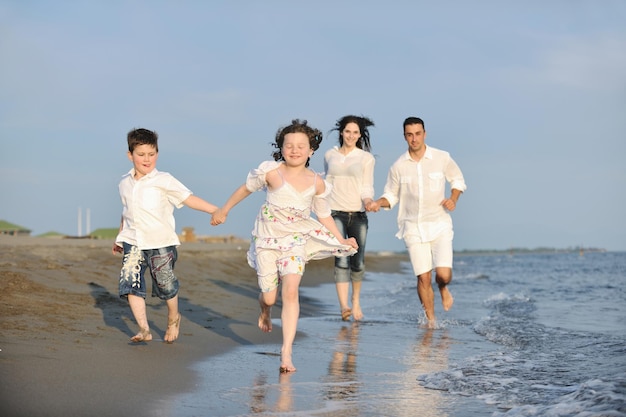 la familia joven feliz se divierte en la playa, corre y salta al atardecer