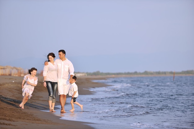 la familia joven feliz se divierte en la playa, corre y salta al atardecer