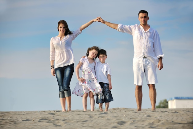 la familia joven feliz se divierte en la playa y muestra el cartel de casa con las manos conectadas mientras protege a los niños