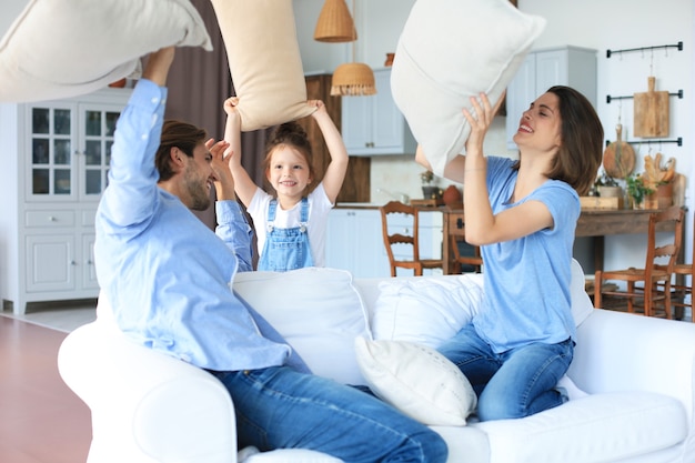 Familia joven feliz divirtiéndose con almohadas en el sofá.