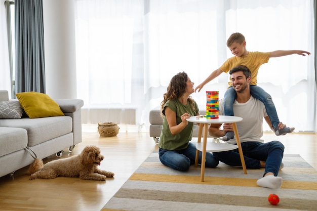 Familia joven feliz divirtiéndose, jugando juntos en casa con perro