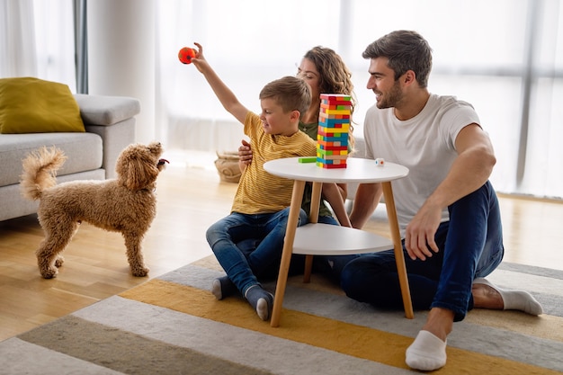 Foto familia joven feliz divirtiéndose, jugando juntos en casa con perro