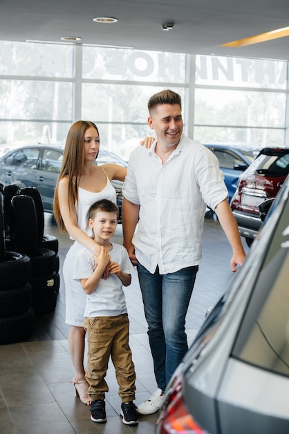 Una familia joven y feliz elige y compra un automóvil nuevo en un concesionario de automóviles. Comprar un auto nuevo.