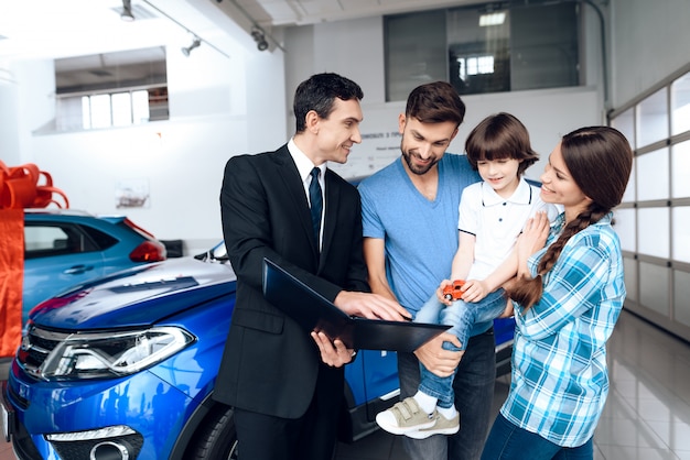 La familia joven feliz está eligiendo un coche nuevo.