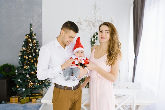 Una familia joven y feliz con un hijo pequeño celebra el año nuevo y celebra la Navidad en el árbol navideño.