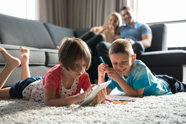 Familia joven feliz jugando juntos en casa en el suelo usando una tableta y un juego de dibujo para niños