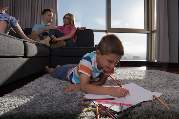 Familia joven feliz jugando juntos en casa en el suelo usando una tableta y un juego de dibujo para niños