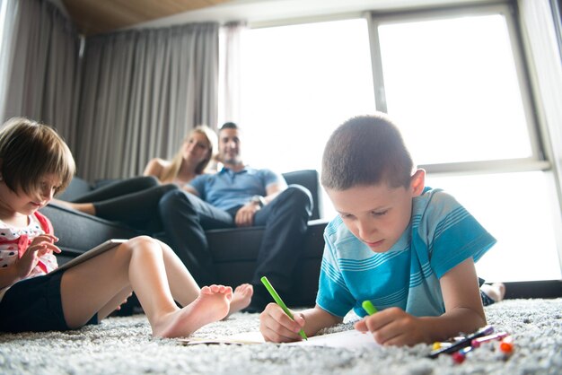 Familia joven feliz jugando juntos en casa en el suelo usando una tableta y un juego de dibujo para niños