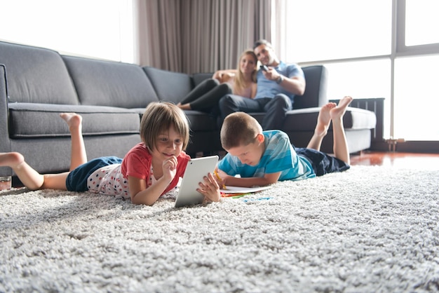 Familia joven feliz jugando juntos en casa en el suelo usando una tableta y un juego de dibujo para niños