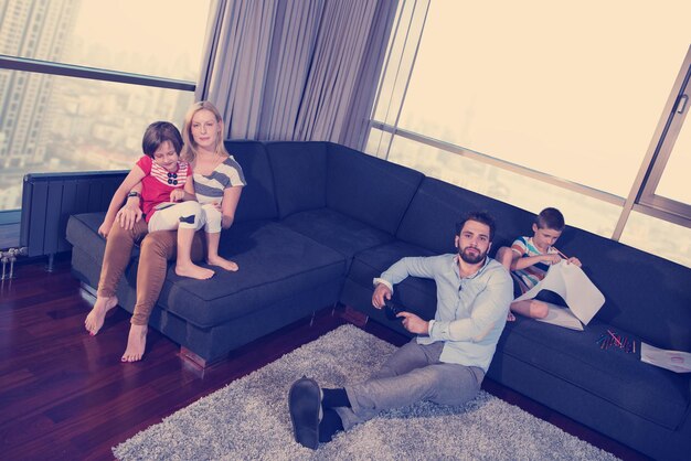 Familia joven feliz jugando juntos en un sofá en casa usando una tableta y un juego de dibujo para niños