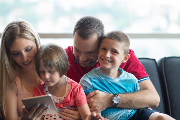 Familia joven feliz jugando juntos con tableta en casa sentado en el sofá