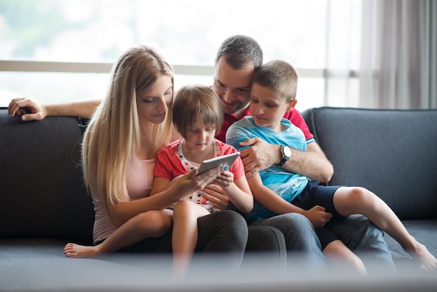 Familia joven feliz jugando juntos con tableta en casa sentado en el sofá