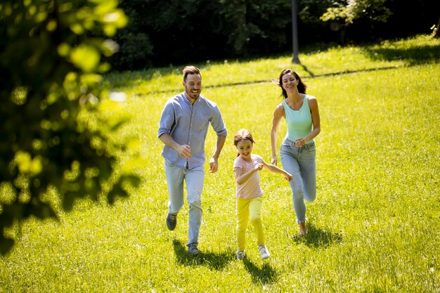 Familia joven feliz con linda hijita corriendo en el parque en un día soleado