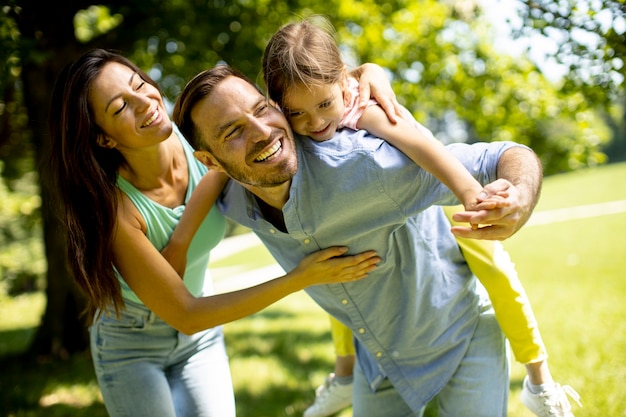 Familia joven feliz con linda hijita divirtiéndose en el parque en un día soleado