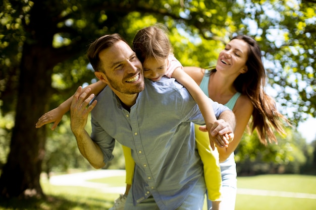 Familia joven feliz con linda hijita divirtiéndose en el parque en un día soleado