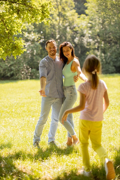 Familia joven feliz con linda hijita divirtiéndose en el parque en un día soleado