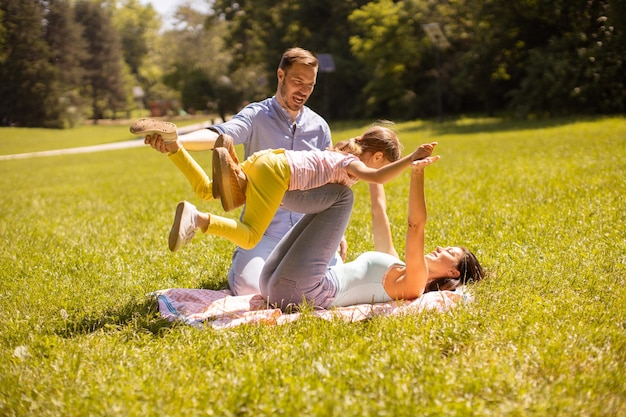 Familia joven feliz con linda hijita divirtiéndose en el parque en un día soleado